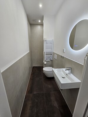 Features a sleek bathroom with a white toilet, sink, and wall-mounted mirror.