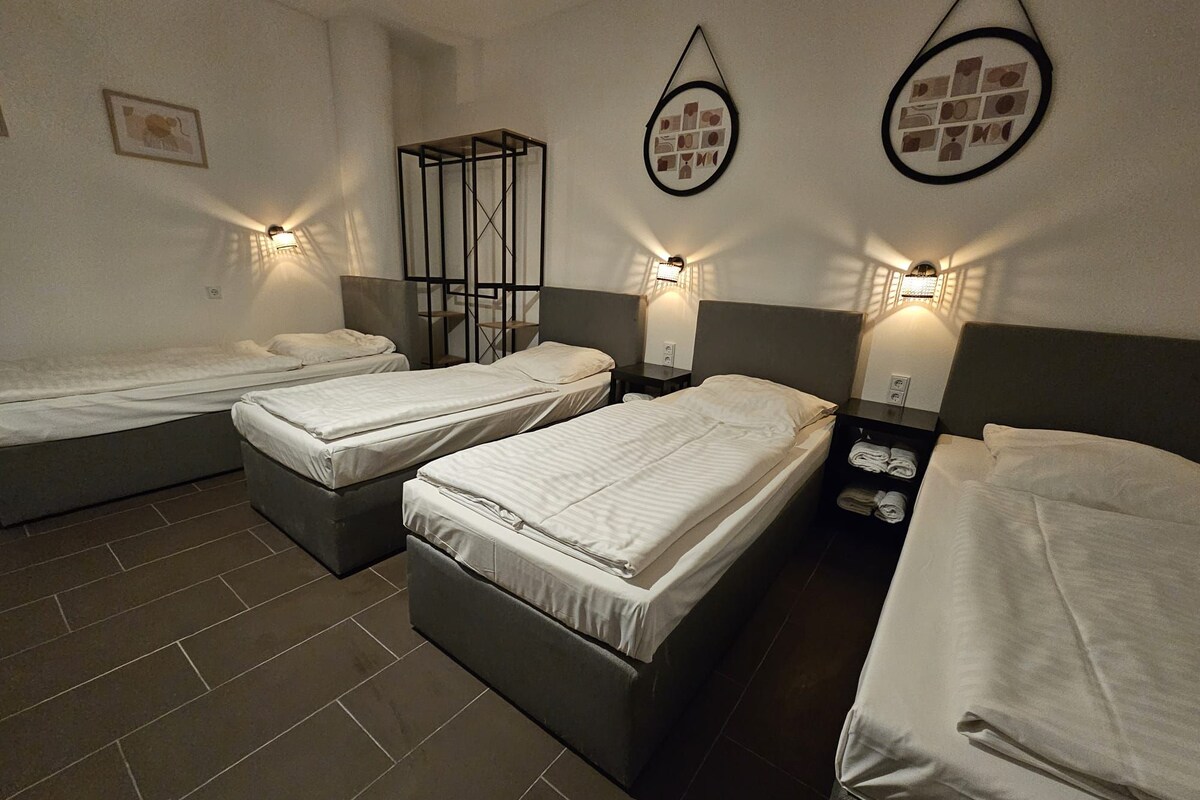 Une chambre d’hôtel avec trois lits simples, une petite table et des appliques murales.