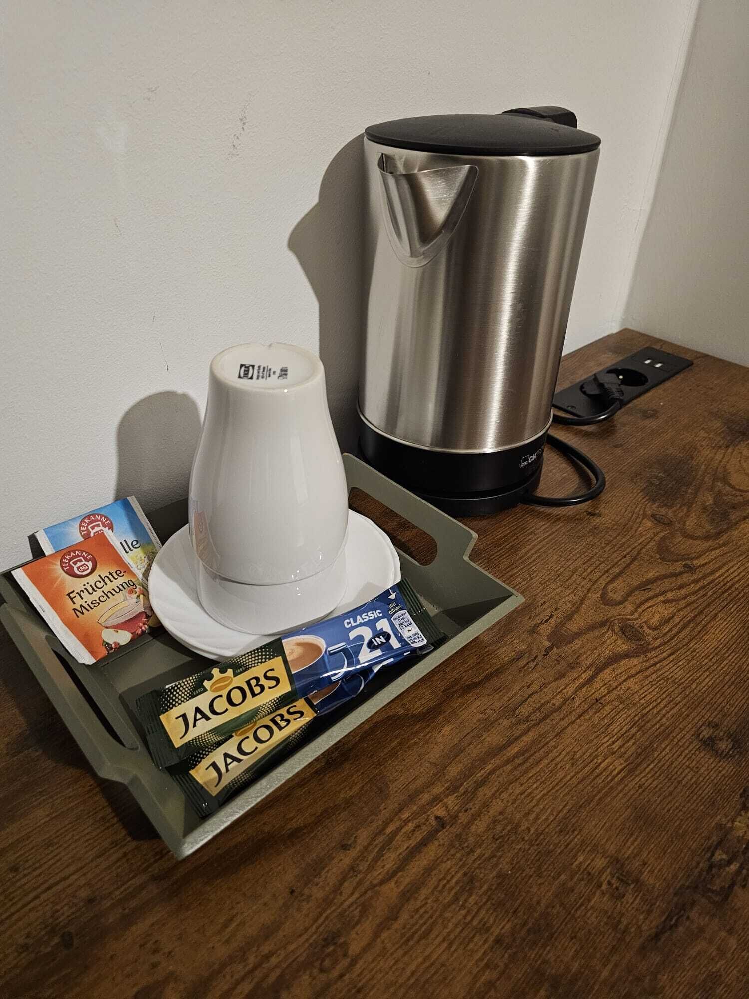 Een koffiezetapparaat, een witte koffiekop en koffiepads op een dienblad.
