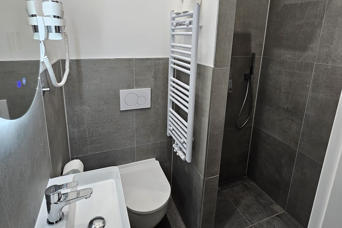 Ein modernes Badezimmer mit einem weißen Waschbecken, einer Toilette und einer begehbaren Dusche.