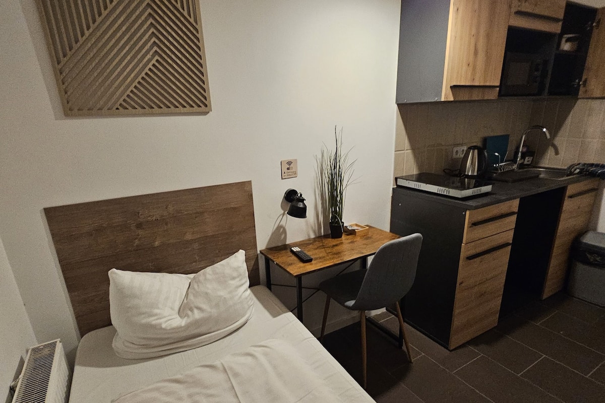 Habitació d'hotel amb llit, escriptori, cadira, petita cuineta i un panell decoratiu a la paret.