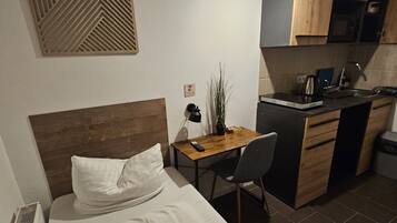 A hotel room with a bed, a desk, a chair, a small kitchenette, and a decorative wall panel.