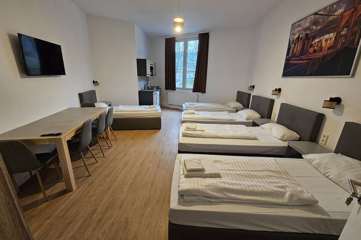 Habitació d'hotel amb escriptori, dos llits individuals, un llit sofà, televisió i finestra amb cortines.