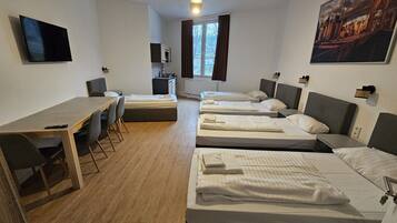Een hotelkamer met een bureau, twee enkele bedden, een slaapbank, een televisie en een raam met gordijnen.