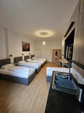 Three single beds with grey headboards and white bedding, a kitchenette, and a large window with city views.