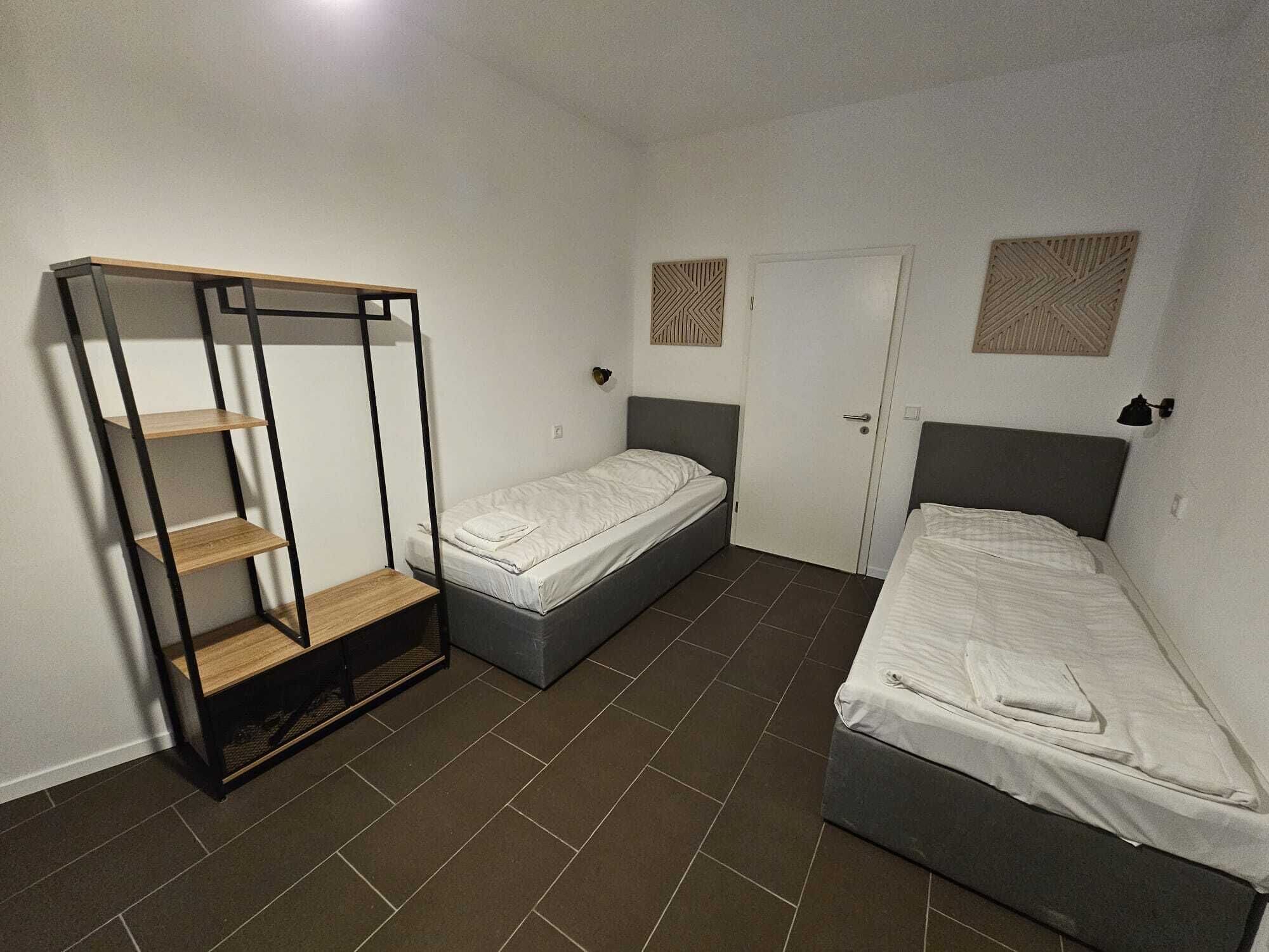 Een kleine kamer met twee eenpersoonsbedden, een garderobe met planken en een deur met decoratief patroon.