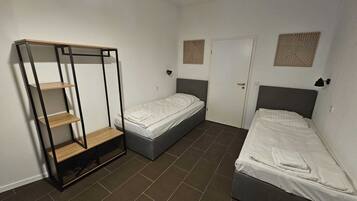 Een kleine kamer met twee eenpersoonsbedden, een garderobe met planken en een deur met decoratief patroon.