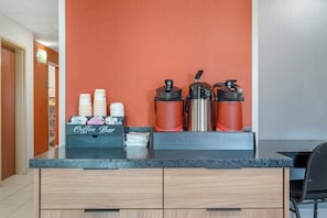 A coffee bar with a coffee maker, a hot water dispenser, and a thermos. There are stacked paper cups and a coffee station sign. - Red Roof Inn Charlestown (Charlestown)