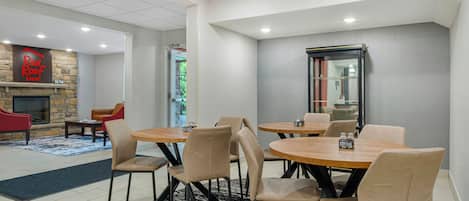 A hotel lobby with a fireplace, seating area, and a dining space with round tables and chairs.