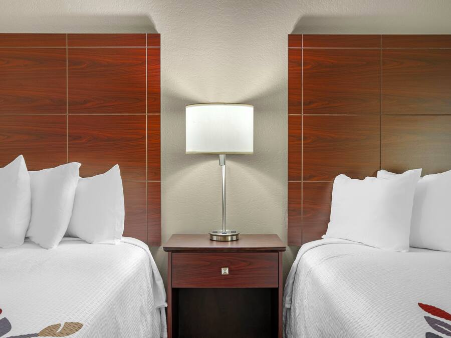 Habitación de hotel con dos camas, una mesita de noche con lámpara y cabecero de madera.