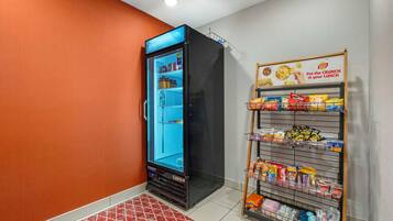 Habitación de hotel con minibar, un refrigerador lleno de bebidas y una alacena con diferentes papas fritas y aperitivos.