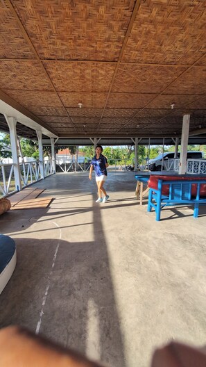 An outdoor covered area with a concrete floor, a wooden ceiling, and a blue table with a red cushion.