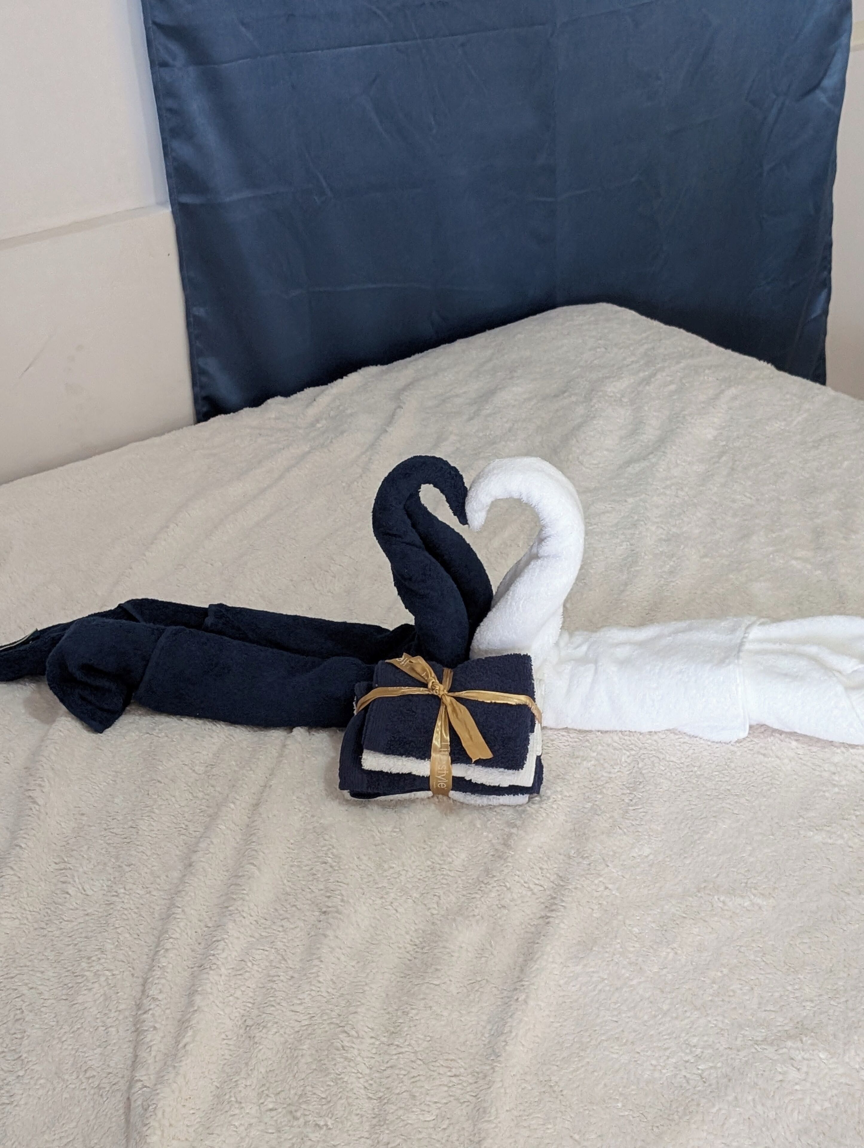A bed with a beige blanket and two towels, one black and one white, tied with a gold ribbon.