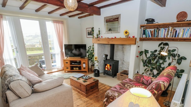 A cozy living room with a sofa, a coffee table, a fireplace, a television, and a bookshelf. - Serenity Cottage (Keighley)
