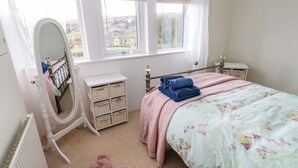 A bedroom with a bed, a dresser, a mirror, and a window with a view of the countryside. - Serenity Cottage (Keighley)