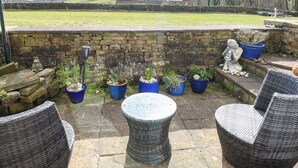 A patio with wicker furniture, stone walls, and potted plants. - Serenity Cottage (Keighley)