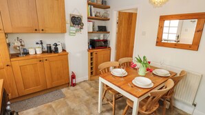 A cozy kitchen with wooden cabinets, a dining table set for four, and a mirror on the wall. - Serenity Cottage (Keighley)