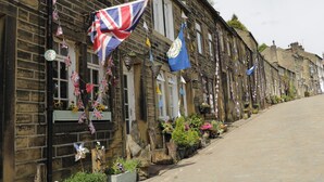A row of traditional stone buildings with flags and flowers. - Serenity Cottage (Keighley)