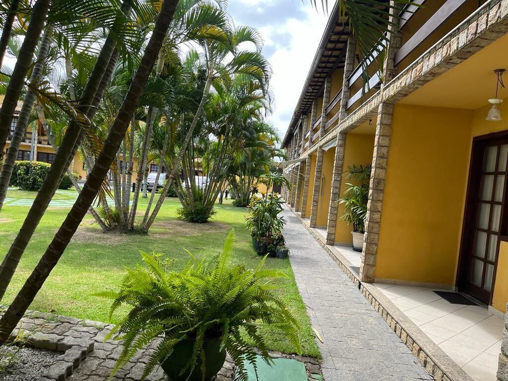 Corredor de hotel com fachada amarela, pilares de pedra e um gramado verde com palmeiras.