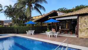 Una piscina con deck de baldosas, mobiliario exterior blanco y sombrillas azules.