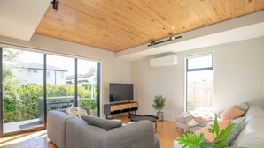 Ein modernes Wohnzimmer mit einem grauen Sofa, einem weißen Couchsofa und einem Fernseher auf einem Holzgestell.