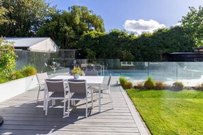 Une terrasse avec une table et des chaises, une clôture en verre et une piscine.