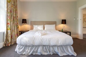 Une chambre d’hôtel avec un grand lit, deux tables de chevet, une tête de lit et un rideau orné d’un motif floral.
