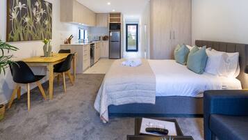 Een moderne hotelkamer met een bed, nachtkastje en uitzicht op de keuken en eetruimte.