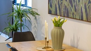 Un espacio de oficina moderno con una mesa de madera, sillas negras, un jarrón con flores amarillas y un cuadro de flores blancas en la pared.