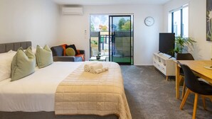 Un dormitorio con cama, escritorio y silla. Hay una ventana y una puerta que da a un espacio exterior.