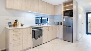 Una cocina moderna con armarios de madera clara, un refrigerador de acero inoxidable y un horno empotrado.