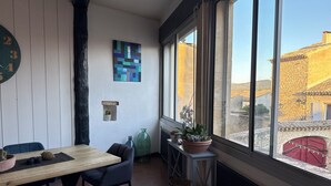 Una habitación acogedora con una mesa de madera, sillas, una planta en maceta y vistas a un edificio a través de amplios ventanales.