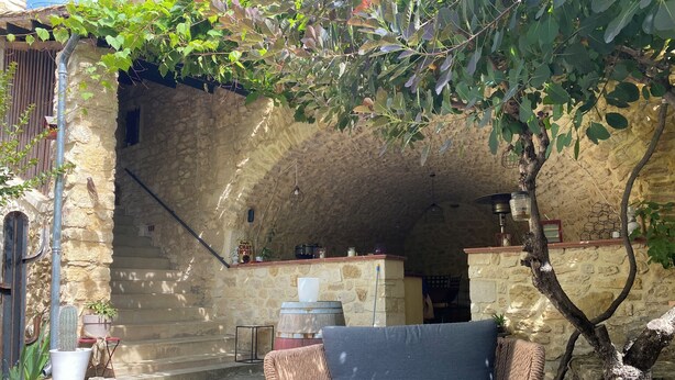 Un espacio al aire libre con paredes de piedra, una silla de mimbre, una planta en maceta y un banco de piedra rústico.