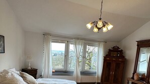 Un dormitorio con dos camas, suelo de madera, candelabro, ventana grande con cortinas y vistas al exterior.