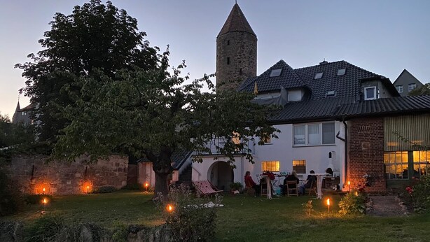Una casa grande con una torre, rodeada de un jardín cuidado y un pequeño espacio de juegos.