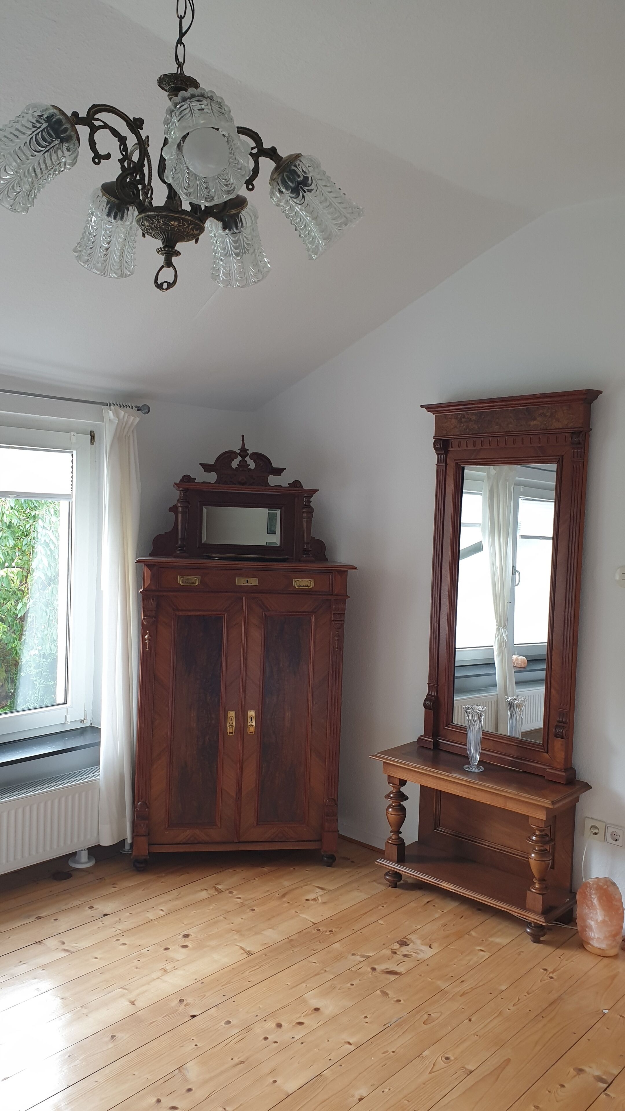 A room with a wooden cabinet, a mirror, and a chandelier.