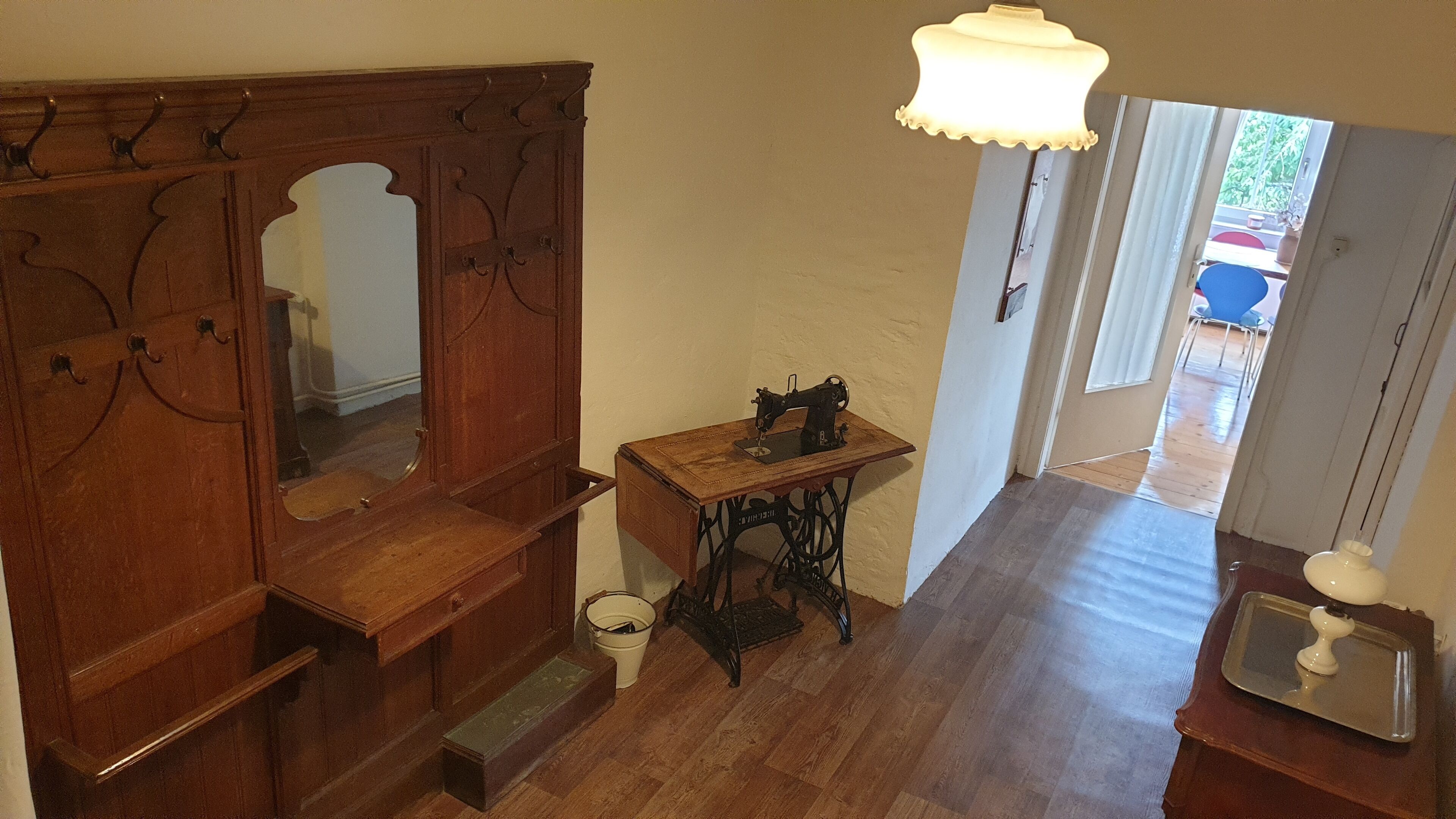 A room with a wooden cabinet, a sewing machine, a mirror, and a small table with a lamp.