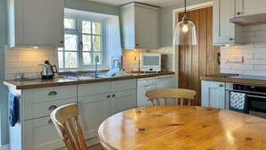 A kitchen with a wooden table, white cabinets, a microwave, and a hanging light fixture. - Derwent Cottage - UK49220 (Burythorpe, near Malton)