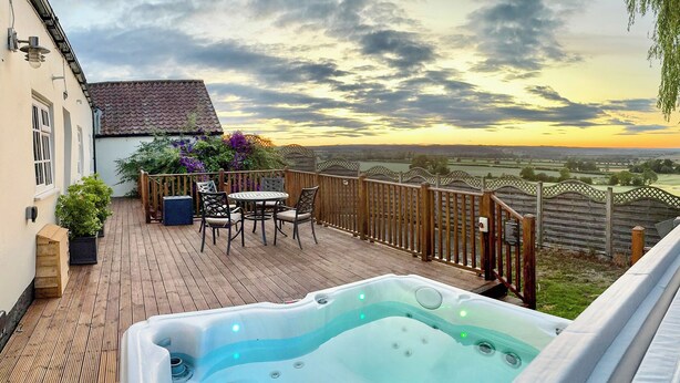 A hot tub on a wooden deck with a view of a sunset and countryside. - Derwent Cottage - UK49220 (Burythorpe, near Malton)