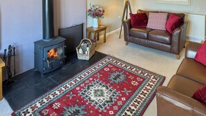 A cozy living room with a fireplace, a brown leather sofa, a patterned rug, and a framed landscape painting. - Derwent Cottage - UK49220 (Burythorpe, near Malton)