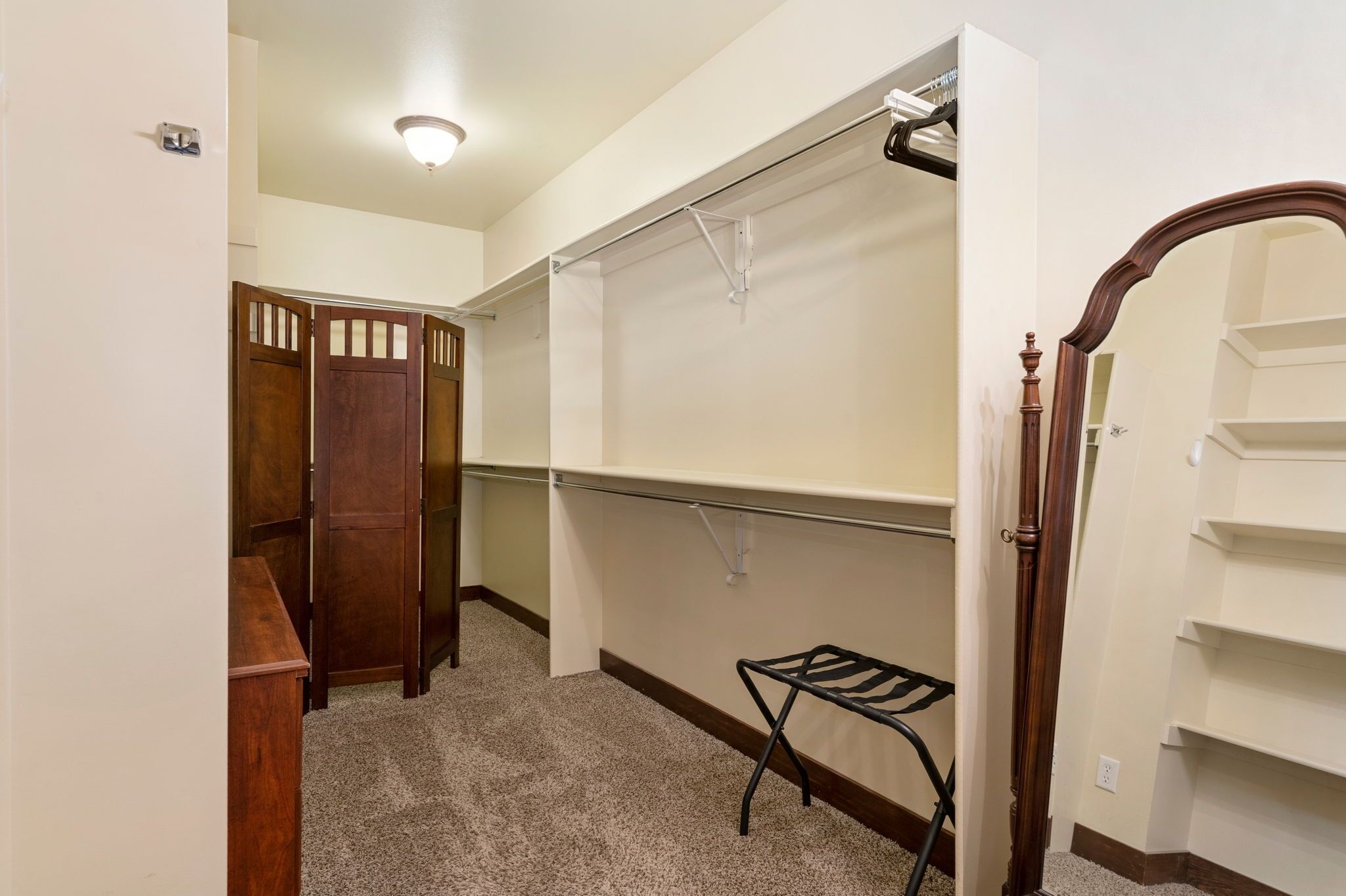 Un couloir avec une porte en bois, un porte-manteau, une petite étagère en métal noir et un mur blanc agrémenté d’un luminaire.