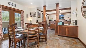 Un comedor con una mesa redonda y sillas, una cocina con armarios de madera, y una sala de estar con sofá y televisor.