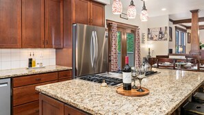 Una cocina con gabinetes de madera, un refrigerador de acero inoxidable, encimeras de granito y una botella de vino.