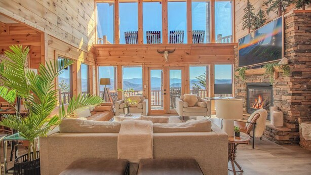 A spacious wooden interior with a large seating area, a fireplace, and a balcony with a scenic view.