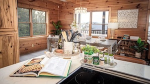A wooden cabin interior with a kitchen area, dining table, and large windows.