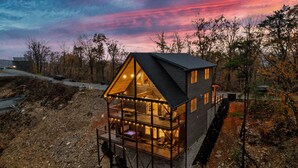 Eine Hütte mit großem Balkon und einer umlaufenden Terrasse, umgeben von Bäumen und einem Feldweg.