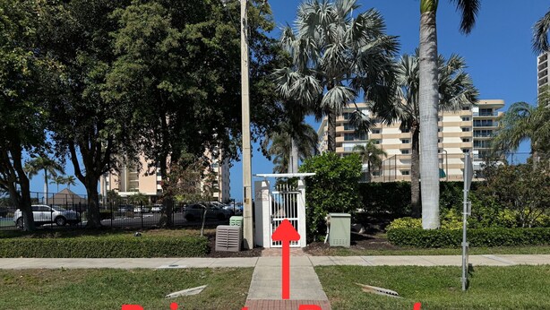 A private beach entrance with a clear pathway leading to a gated area, surrounded by palm trees and residential buildings. - Top-Floor Partial Gulf View!  Steps from the Beach!  Little Tropical Paradise! (Marco Island)
