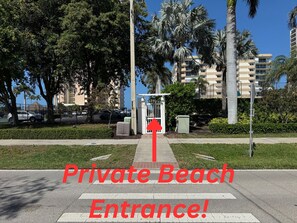 Acesso privado à praia, com um caminho bem definido que leva a uma área murada, cercada por palmeiras e edifícios residenciais.