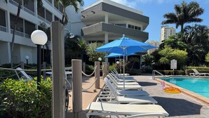 A poolside area with lounge chairs, a blue umbrella, and a sign indicating pool rules. - Top-Floor Partial Gulf View!  Steps from the Beach!  Little Tropical Paradise! (Marco Island)
