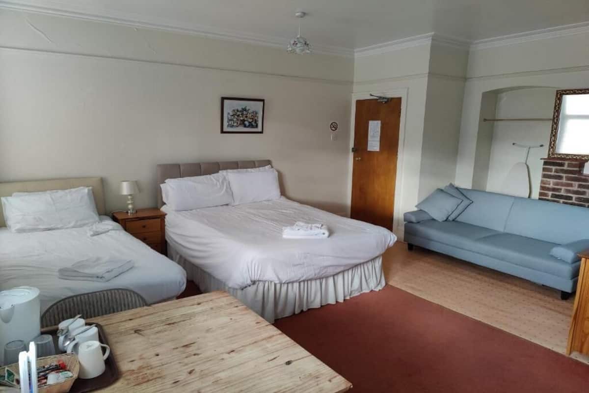 A hotel room with two beds, a sofa, a wooden table, and a mirror.